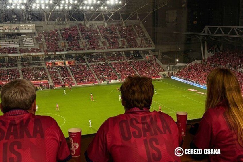 A stadium with spectators wearing red jackets, a soccer field, and a large crowd. 2