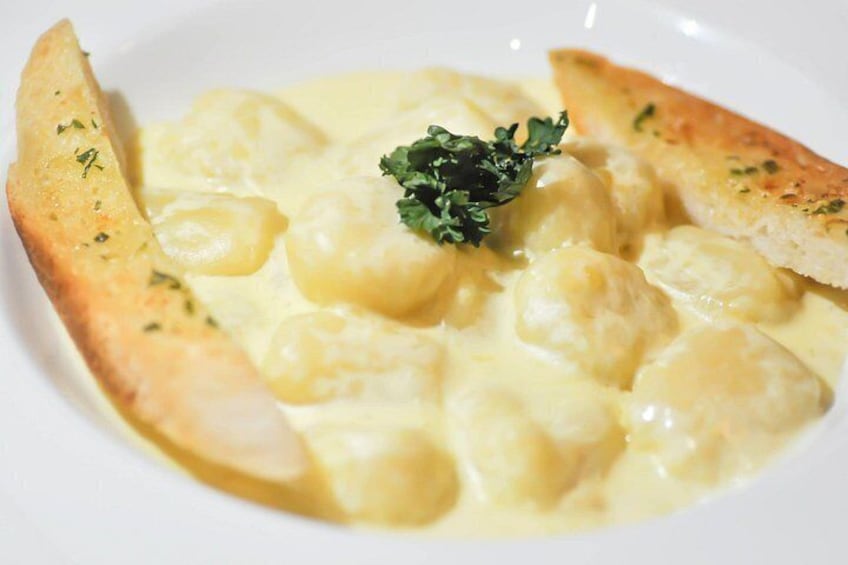 Een bord gnocchi met romige saus, bestrooid met peterselie, en vergezeld van een sneetje geroosterd brood. 2