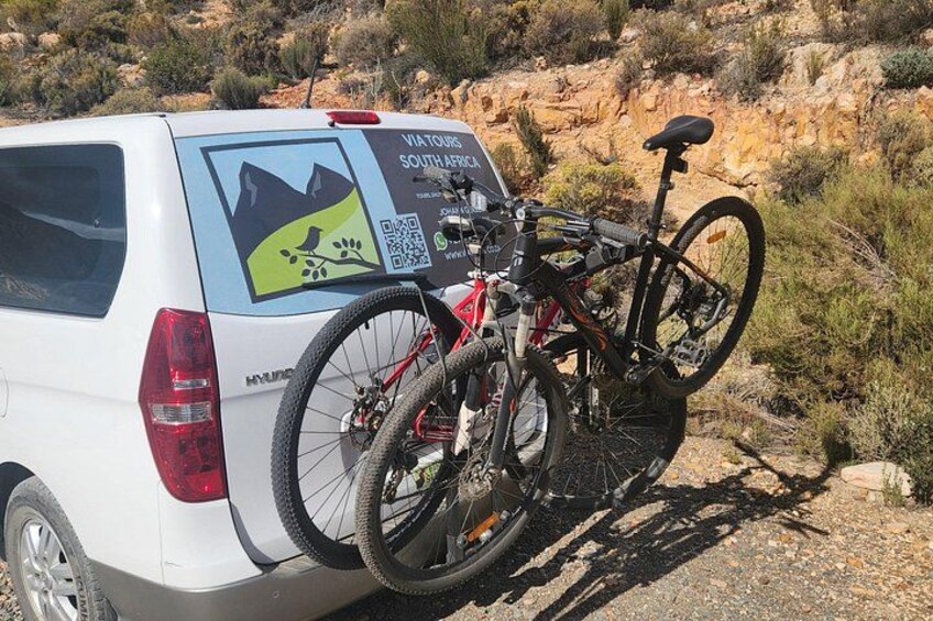 En hvid varevogn med cykelholder, en cykel og et skilt, der angiver en rundtur i Sydafrika. 3