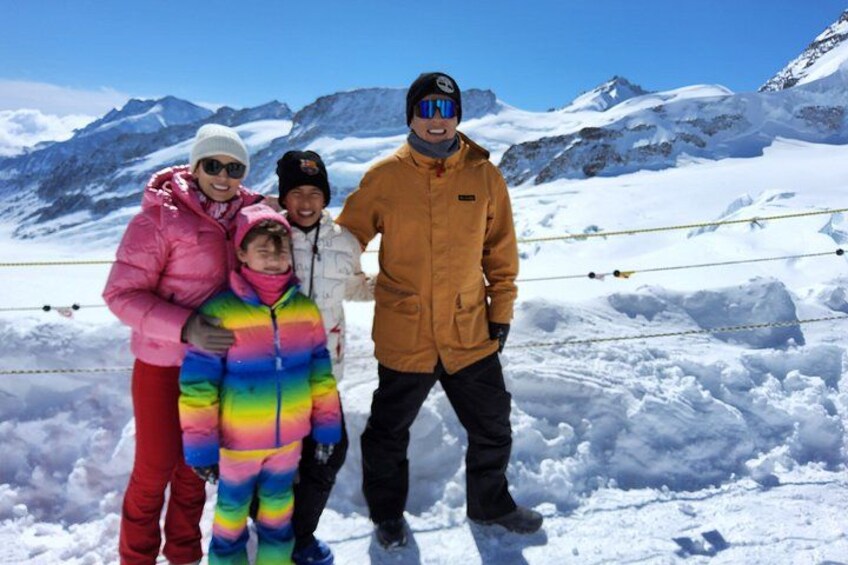 A group of people in winter clothing standing on a snowy mountain with a clear sky. 4