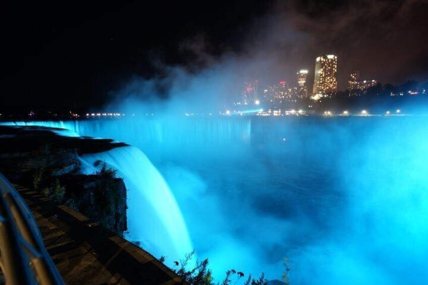 A night-time waterfall illuminated by blue lights, with a city skyline in the background. 5