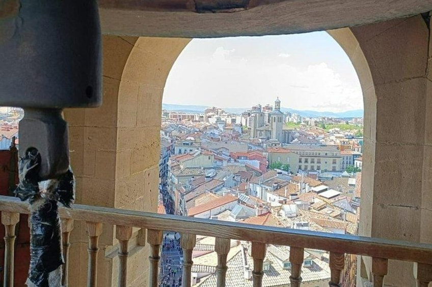 A view from a balcony with a stone railing, overlooking a cityscape with buildings and a distant mountain range. 1