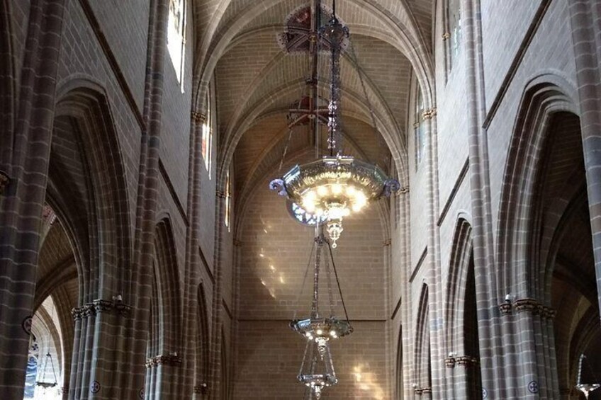 Et katedralinteriør med hvælvede lofter, buede vinduer og hængende lysekroner. 2