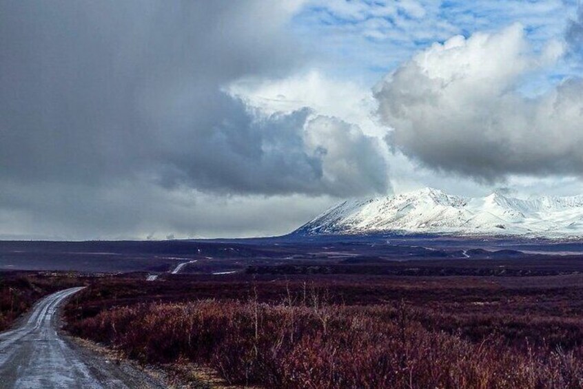 A snow-covered mountain, a dirt road, and a cloudy sky. 3
