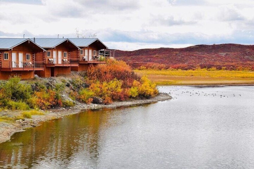 A lakeside lodge with wooden cabins, autumn foliage, and a distant mountain range. 1