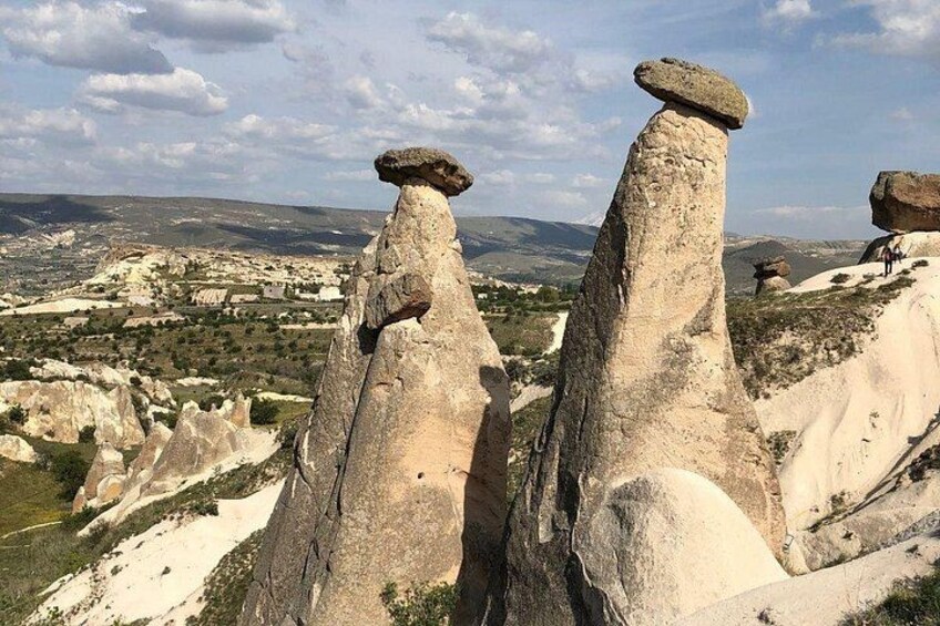 Rock formations with balanced stones on top, a valley with scattered houses, and a cloudy sky. 3