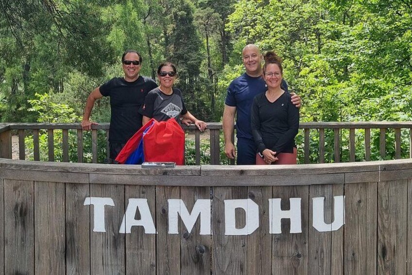A wooden fence with the inscription 'TAMDHU' and a group of people standing behind it. 5