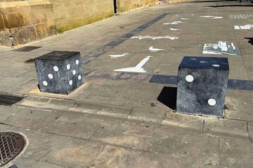 A paved area with two black blocks with white dots, a drainage grate, and white directional arrows. 5
