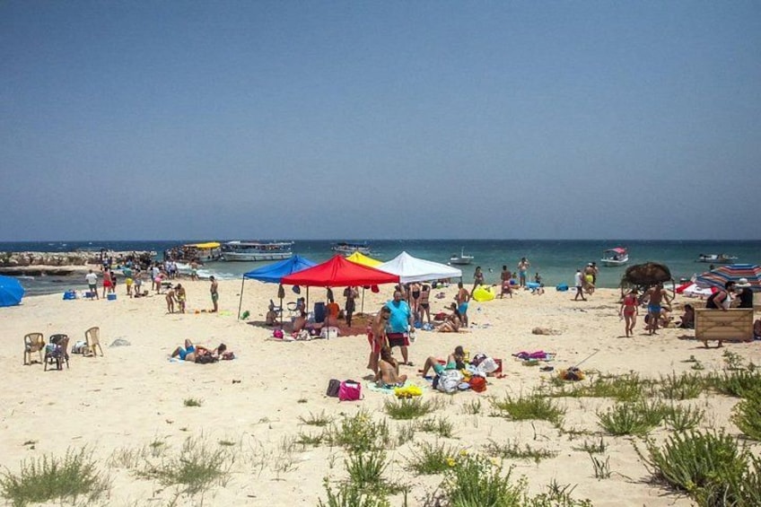 A crowded beach with people sunbathing, umbrellas, and boats in the water. 3