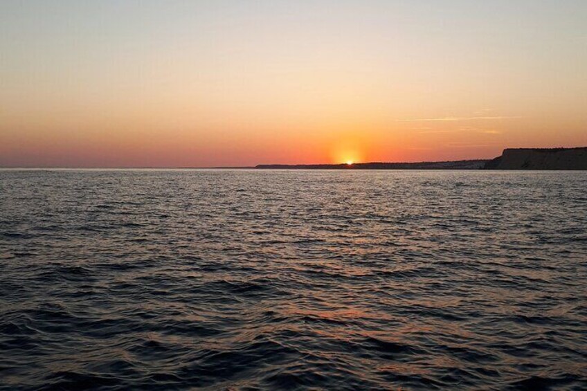 Un coucher de soleil sur une mer calme, avec une terre lointaine à l’horizon. 1