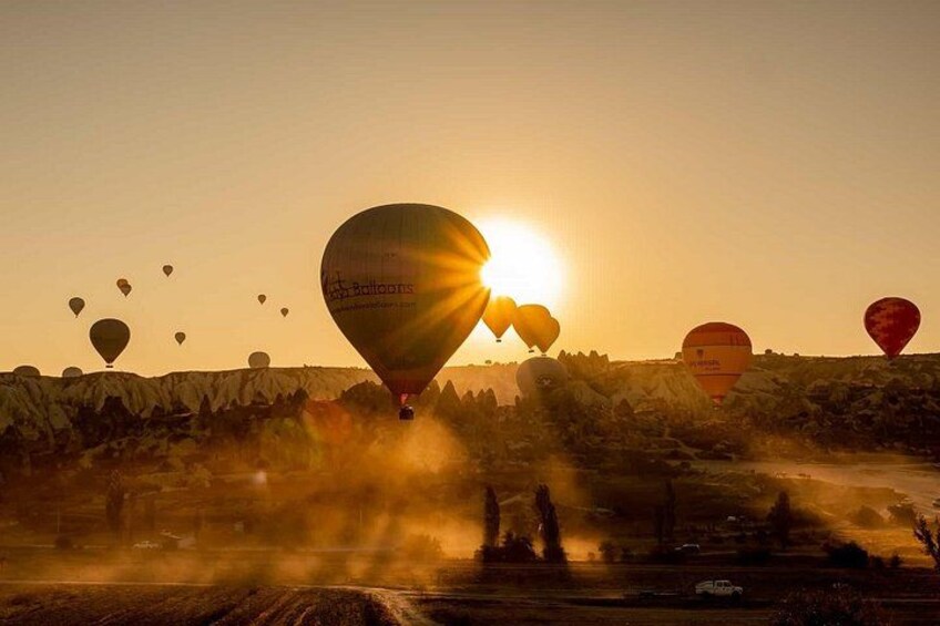 Varmluftsballonger svävar över ett bergigt landskap medan solen går ner i horisonten. 1