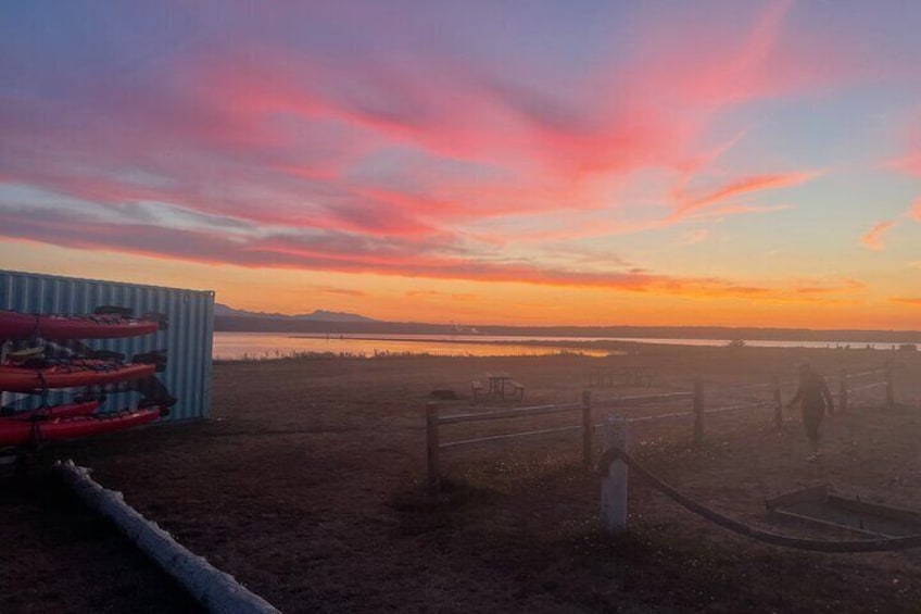 A sunset over a beach with kayaks and a fence. 3