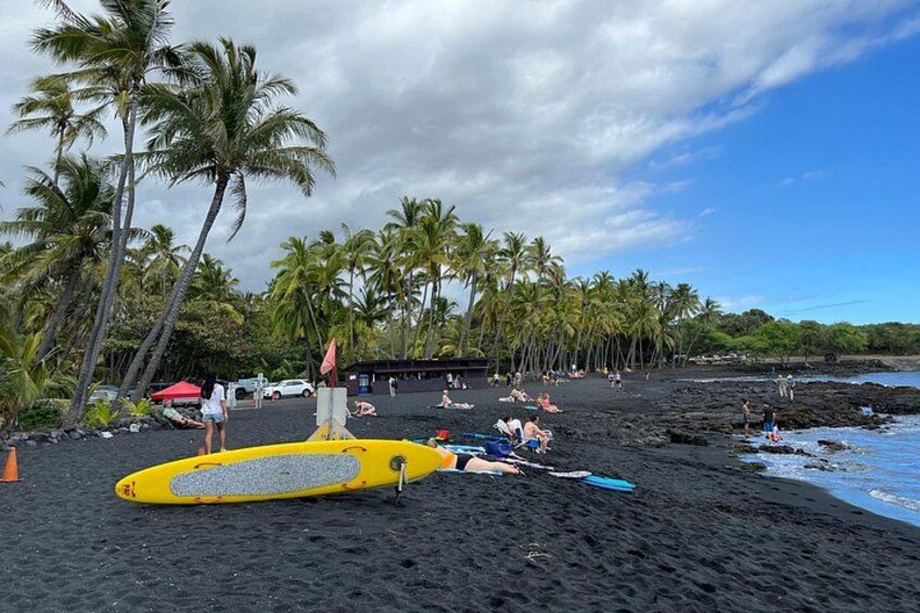 Una spiaggia di sabbia nera con palme, persone che prendono il sole e tavole da surf. 2