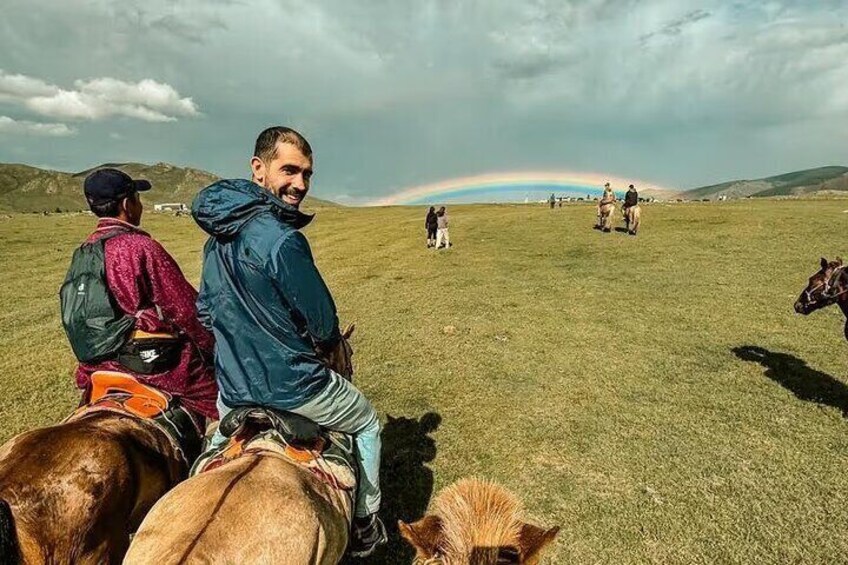 A person riding a horse in a grassy field with a rainbow in the background. 4