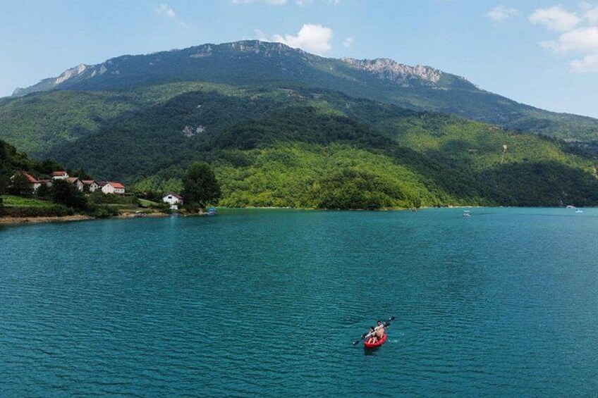Un lago tranquilo con un kayakista, una montaña al fondo y casas en la orilla. 4