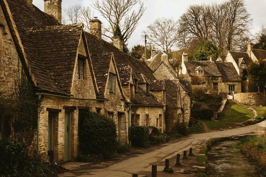 A row of stone houses with steeply pitched roofs, a narrow dirt road, and a small stream. 2