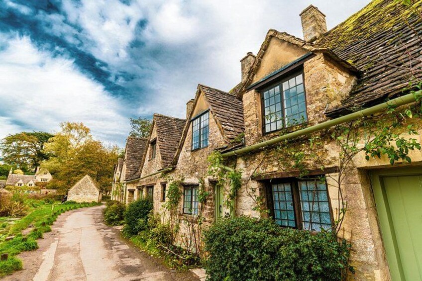 A row of stone houses with green shutters, a narrow path, and lush greenery. 1