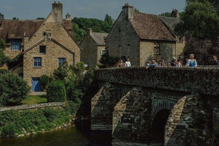A stone bridge with people walking on it, surrounded by stone buildings and greenery. 3