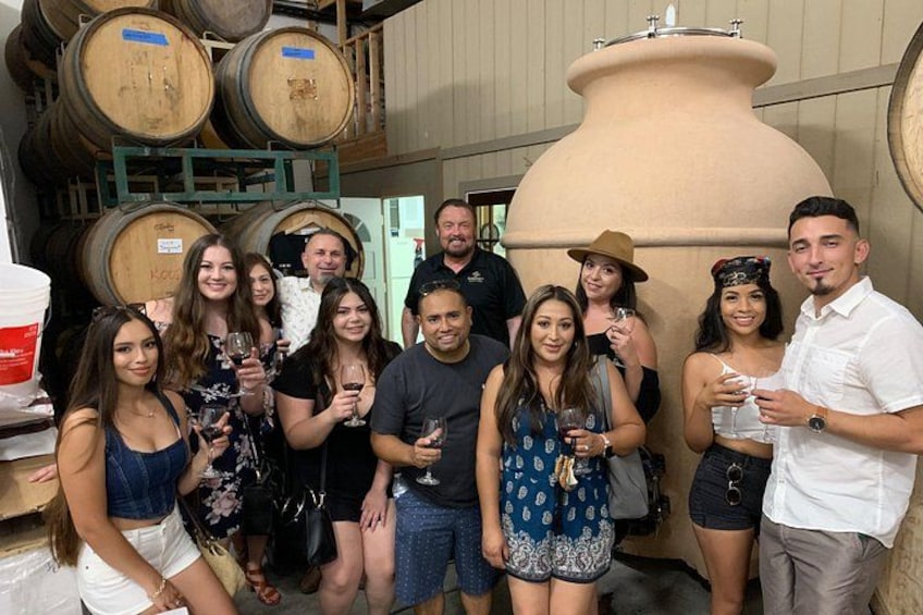 A group of people standing in a wine cellar with barrels and a large fermentation tank. 4
