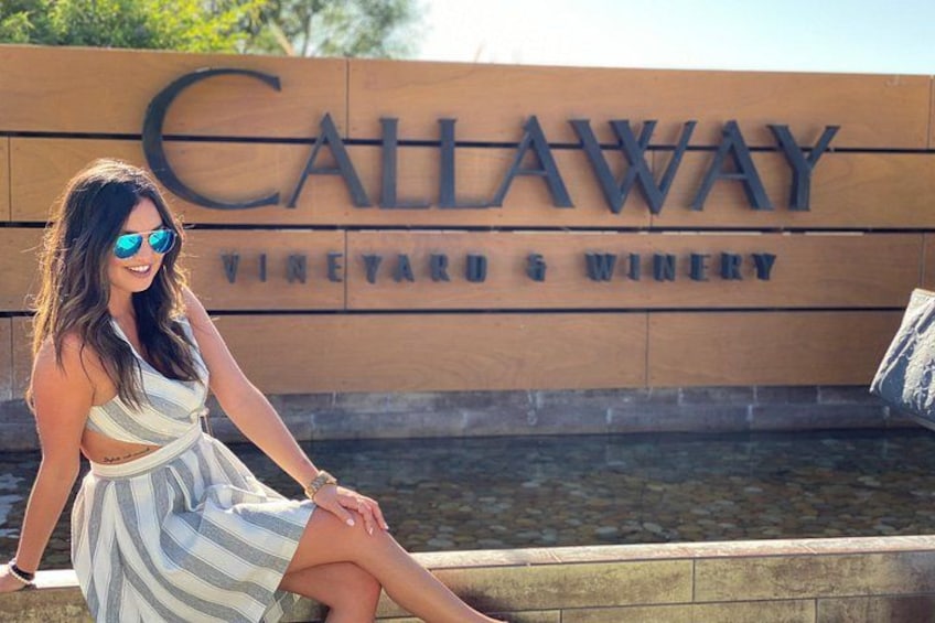 A woman sitting in front of a sign that reads 'Callaway Vineyard & Winery.' 3
