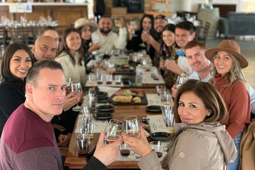 A group of people seated around a long wooden table, holding wine glasses. 5