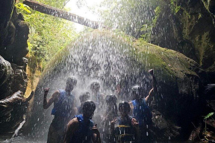 Eine Gruppe von Menschen steht unter einem Wasserfall in einer felsigen Schlucht. 5