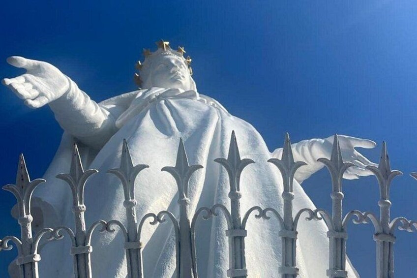 A statue with a crown, dressed in white, standing behind a decorative fence. 2