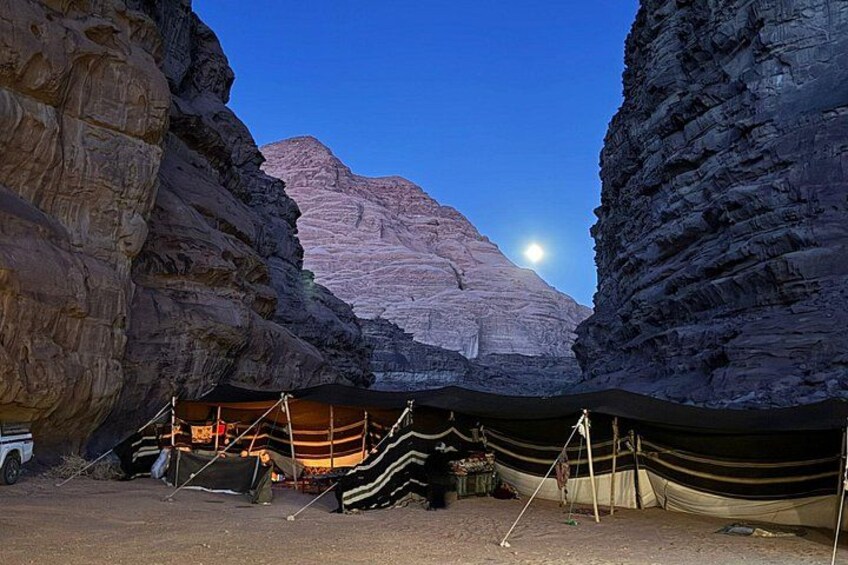 Un campamento con tiendas de campaña y un vehículo en un cañón, con una montaña al fondo. 2