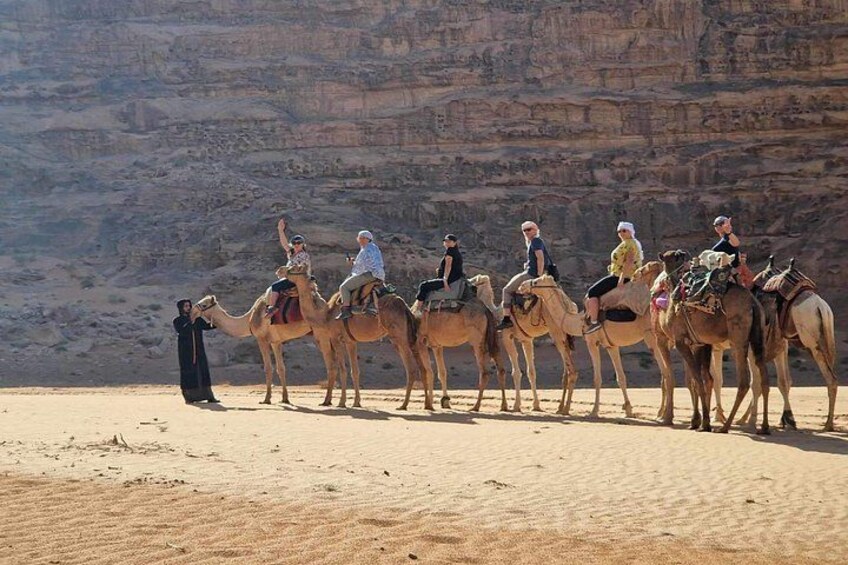 Un grupo de personas montando camellos en un desierto con acantilados rocosos al fondo. 4