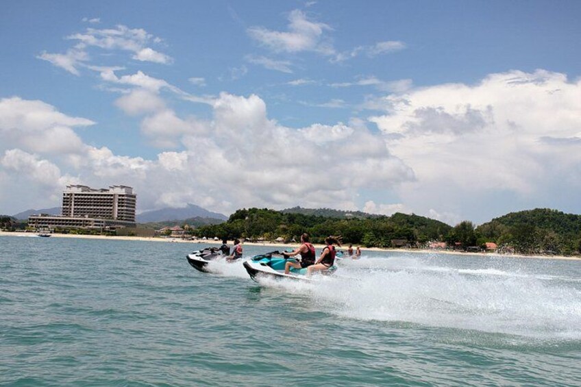 Two jet skis on a calm sea with a hotel and mountains in the background. 2