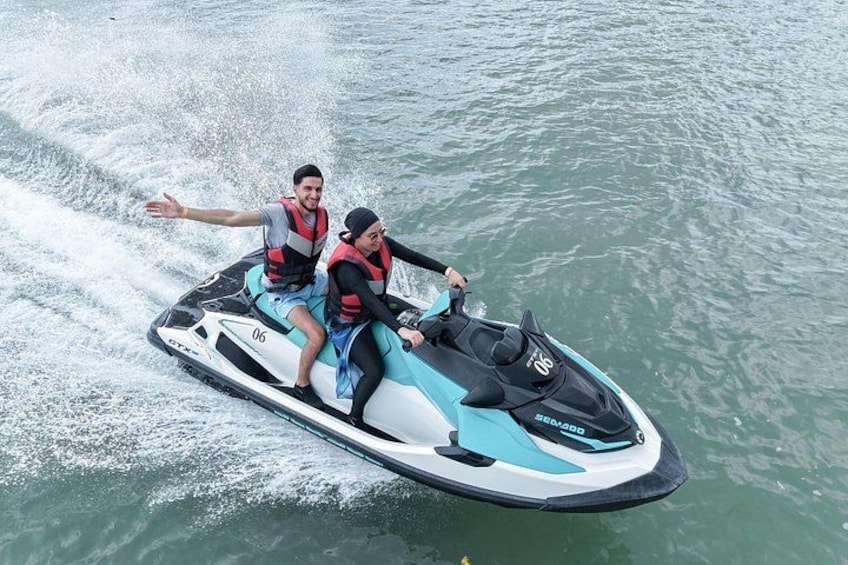 Two people on a jet ski, wearing life jackets, in a body of water. 1