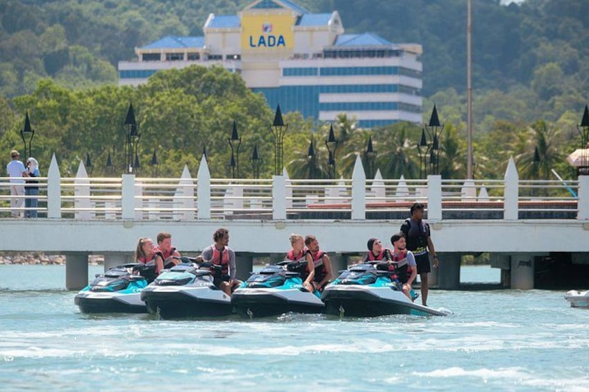 Jet skis on water with people wearing life jackets, a bridge, and a building with 'LADA' on it. 4