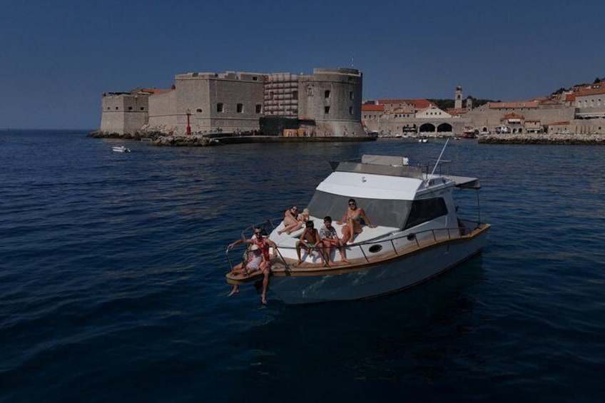 A yacht with passengers on a calm sea, a historic fort in the background, and a clear sky. 4