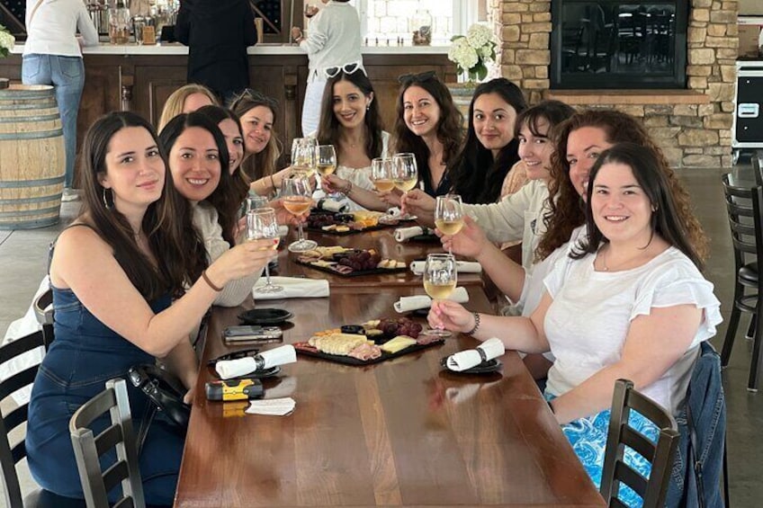 A group of people toasting with wine glasses at a wooden table with food. 1