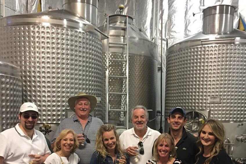 A group of people standing in front of large stainless steel fermentation tanks. 4
