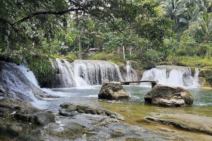 A waterfall, rocks, and a bridge in a forested area. 1