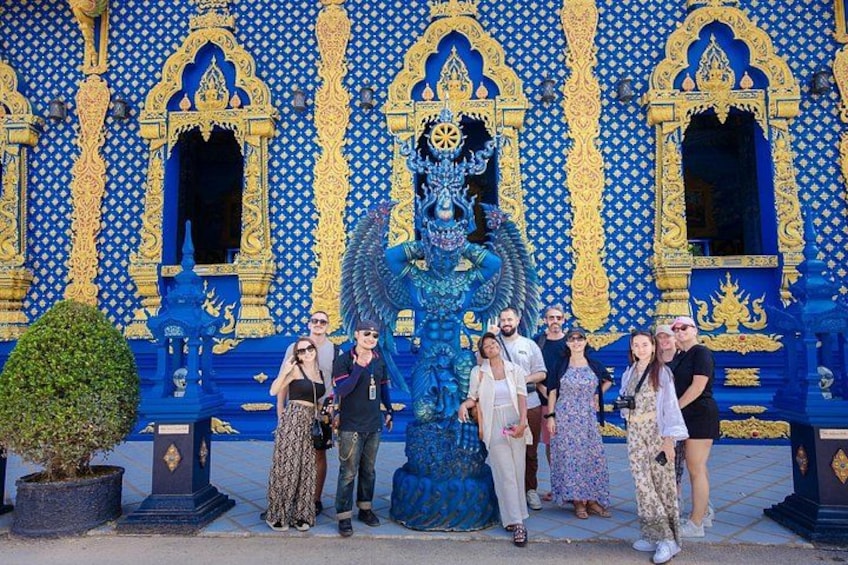 A group of people posing in front of a blue and gold ornate building with a large statue. 4