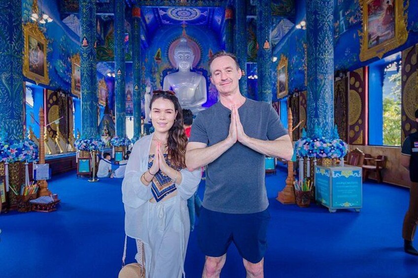 A person in a white dress and another in a grey shirt standing in a room with blue walls and a large statue in the background. 5
