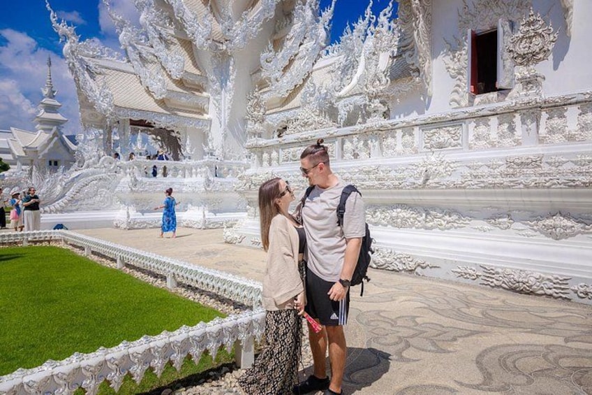 A couple standing in front of a white ornate temple with intricate carvings. 3