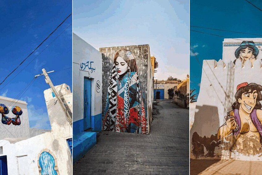 A narrow alley with buildings painted in white and blue, a mural of a woman, and a street sign. 1