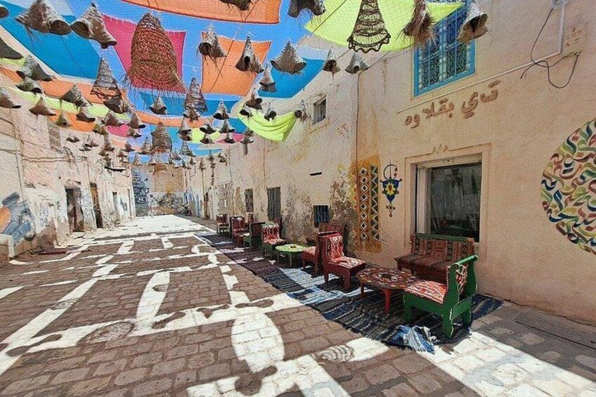 A narrow alley with patterned pavement, colorful hanging decorations, and traditional seating. 2