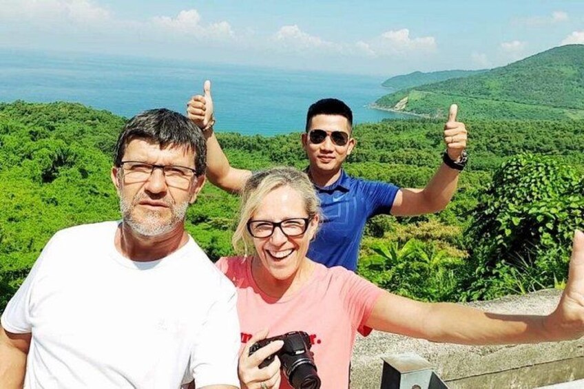 Three people taking a selfie with a scenic view of a lush green landscape and a body of water in the background. 3