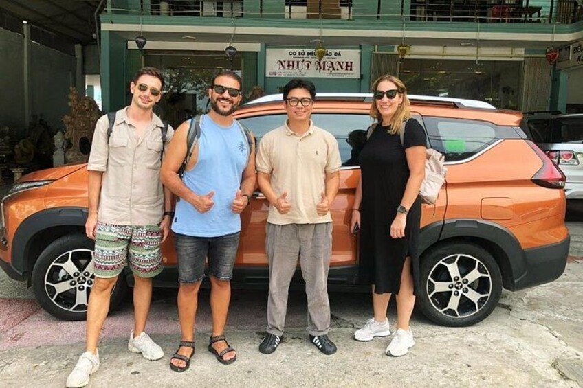 Four people standing in front of an orange car. 2