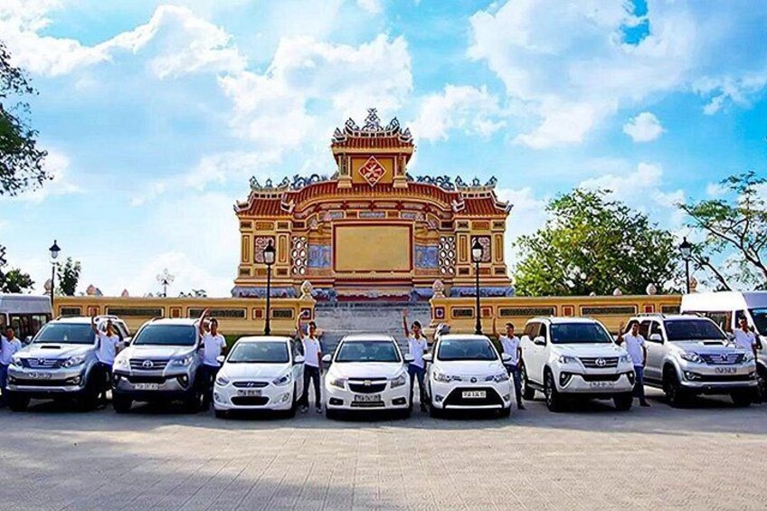 A traditional temple with ornate architecture, a group of white cars parked in front, and a clear blue sky. 4
