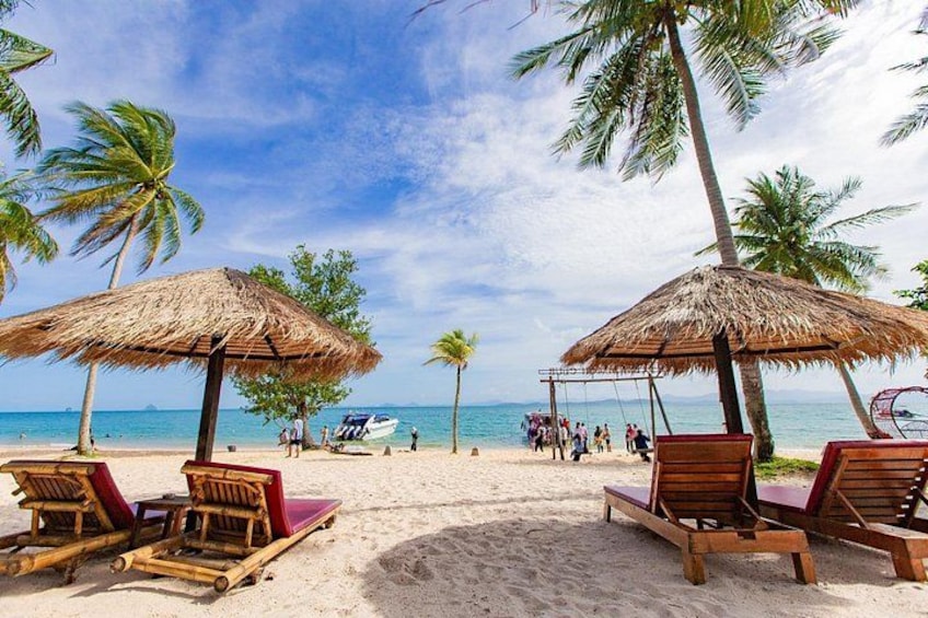 A beach with thatched umbrellas, wooden lounge chairs, palm trees, and a clear sky. 3