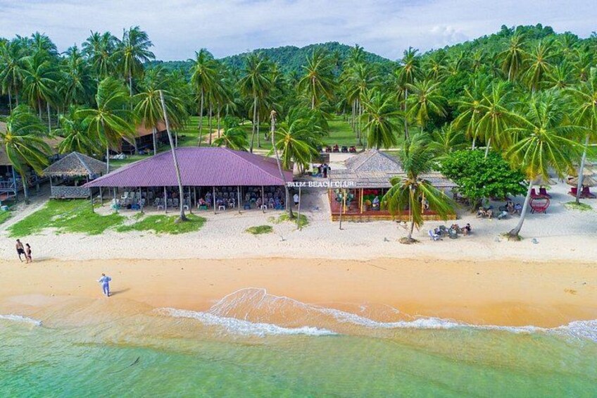 A beach with palm trees, a beach bar, and a thatched-roof building. 2