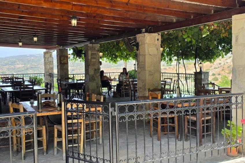Un café al aire libre con mesas y sillas, pilares de piedra y vistas al paisaje. 3