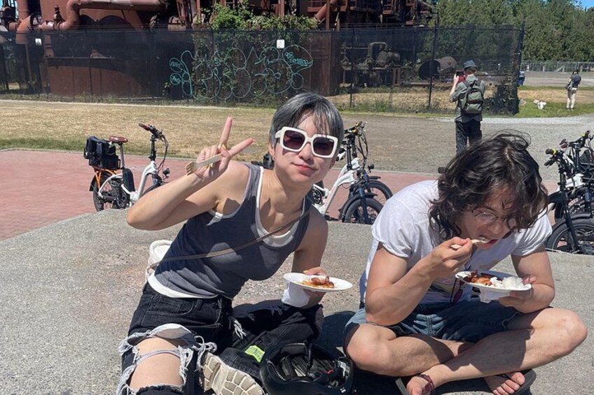 Two people sitting outdoors, one eating and the other making a peace sign. 2