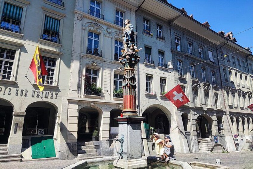 Un edificio storico con una fontana, bandiere e statue. 5