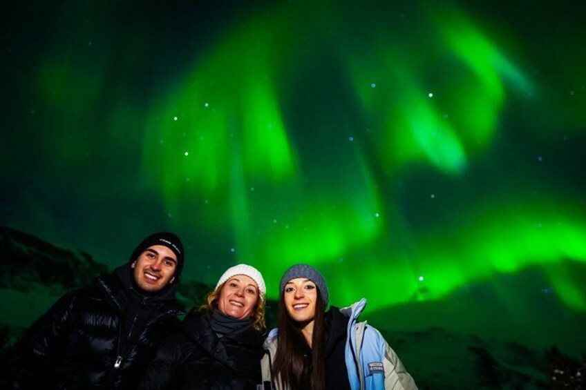 Drie personen staan onder een nachthemel met groen poollicht. 5